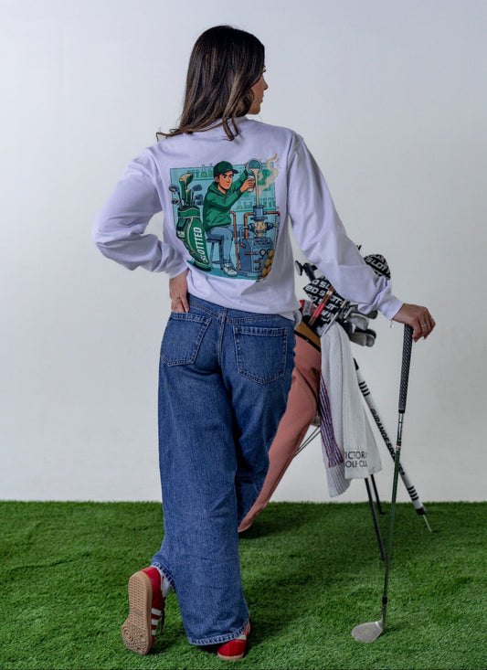 Person wearing a white long-sleeve shirt with a graphic design, standing on grass with a golf club.