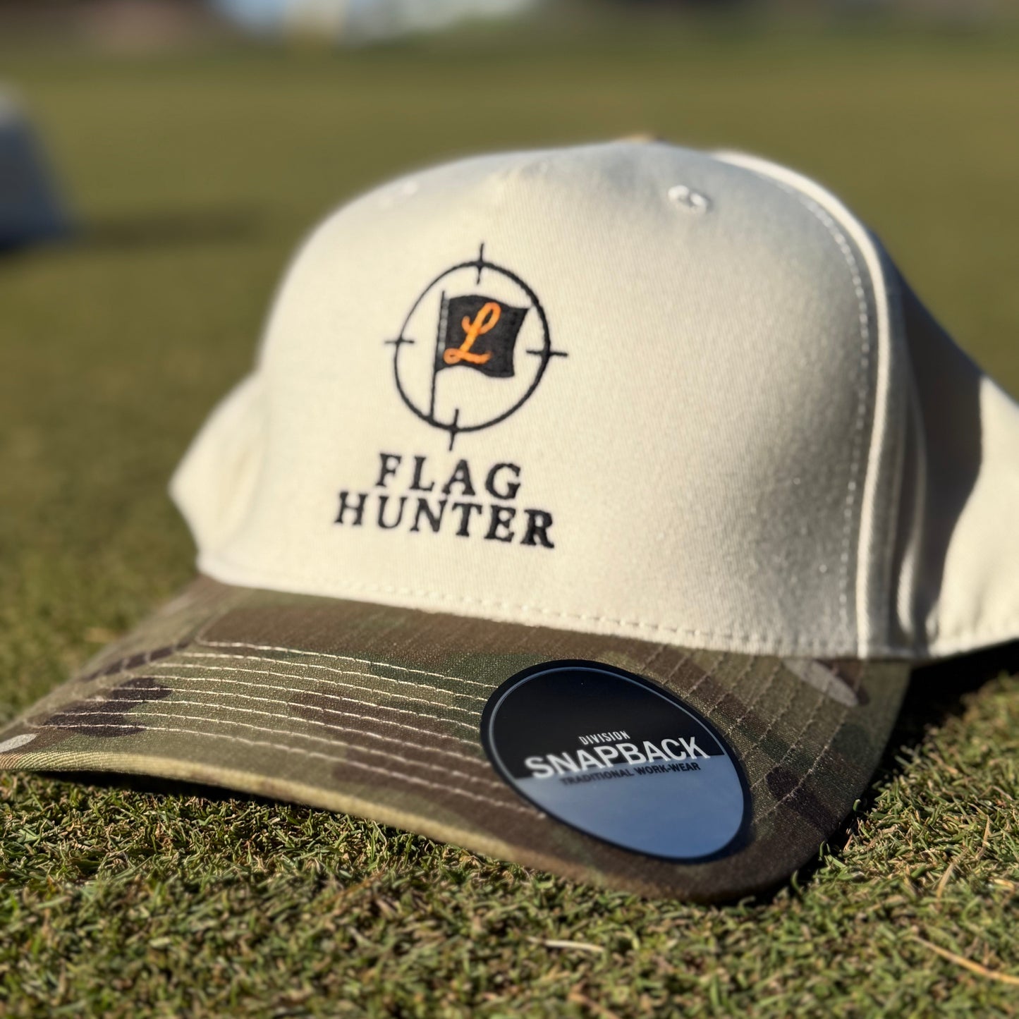 Beige and Camo cap with 'Flag Hunter' logo on a grassy background