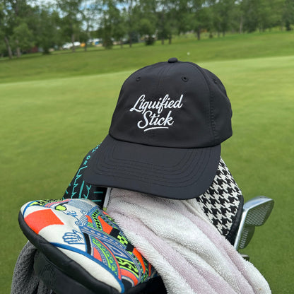 Black cap with 'Liquorished Sticks' logo on a golf bag with a golf club against a green golf course background.