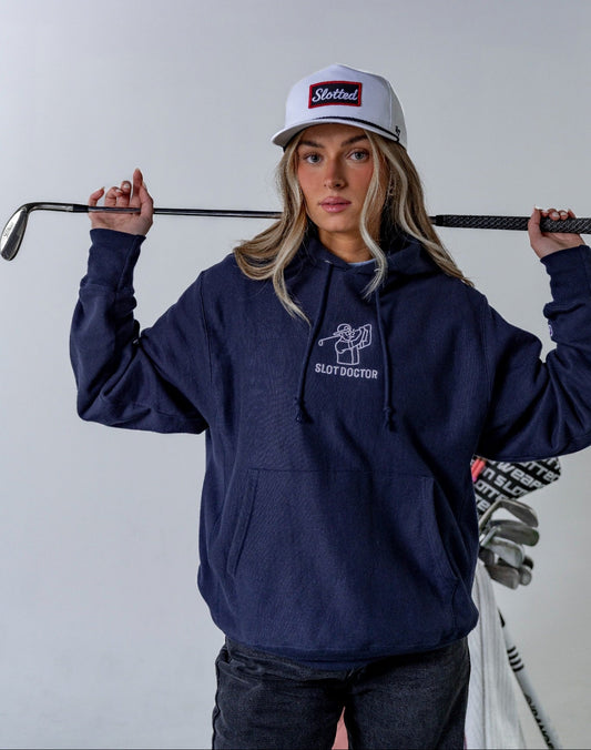 Person wearing a navy hoodie and white cap holding a golf club against a plain background
