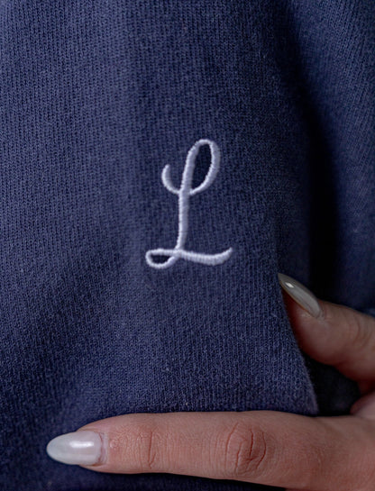 Navy blue fabric with a white embroidered letter 'L' held by a hand.